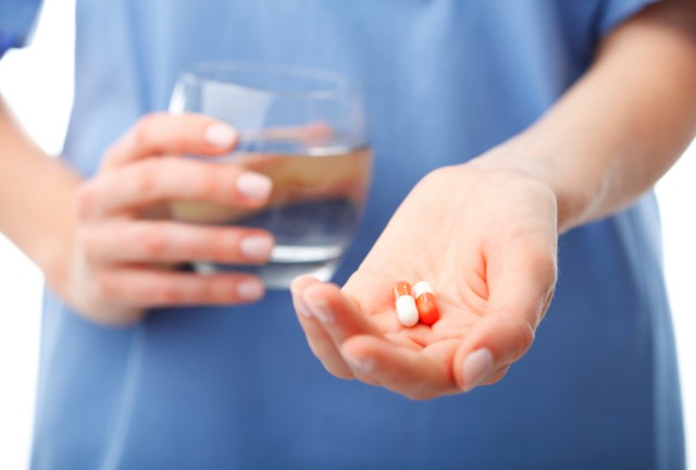 Doctor's hands holding two pills and a glass of water